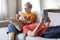 Happy Senior Spouses Relaxing With Modern Gadgets On Couch At Home