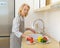 Happy senior woman in apron preparing vegetables for salad while cooking in modern kitchen at home