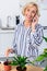 happy senior woman cultivating houseplants and talking by smartphone