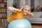 Happy senior woman doing exercises with fitness ball at home, training her back muscles during domestic workout
