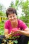 Happy senior woman holding a beautiful pink rose in her hands sitting in blooming summer garden