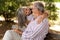 Happy senior woman hugging man in casual, sit on bench, enjoy walk together in park outdoor