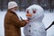 Happy senior woman sculpt and hug a big real snowman in winter
