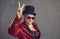 Happy senior woman in sequin outfit, top hat and cool glasses doing V sign gesture