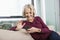 Happy senior woman text messaging through smart phone on sofa at home