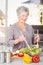 Happy senior woman tossing salad while standing in kitchen