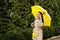 Happy senior woman in yellow rain coat with yellow umbrella is talking on a smartphone and walking in park. Staying in