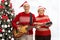 Happy seniors playing a guitar in front of a Christmas tree