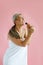 Happy silver haired Asian lady sings with brush standing on pink background