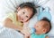 Happy sister feeding milk from bottle for her brother and lying on the bed