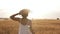 Happy, slender girl in straw hat and summer white dress happily running in clear wheat field. Sun shines on the