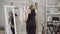 Happy slim Caucasian woman admiring reflection in mirror posing in elegant black dress and beret. Stylish young tailor