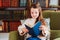 Happy smart schoolgirl reading books in library or at home