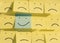 Happy smiley face on a blue sticky note surrounded by sad unhappy yellow faces