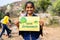 Happy smilig kid holding save environment sign board while other kids cleaning around at hill top - concept of support