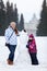 Happy and smiling adult woman and young girl standing near snowman on wintry field of park, winter time