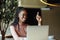 Happy smiling afro american woman sitting on table pointing finger up and working online in coffee house. Black girl