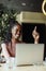 Happy smiling afro american woman sitting on table pointing finger up and working online in coffee house. Black girl