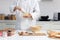 Happy smiling Asian man in white chef uniform with hat, stirring and mixing eggs in glass bowl. young baker man cooking meal food