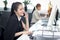 Happy smiling Asian woman officer sitting, talking on mobile phone at office desk with blurred busy colleague background, modern