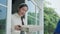 Happy smiling Asian woman receives carton box of food from courier in front house. Delivery man in red uniforms deliver express.