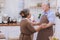 Happy & smiling attractive elderly cute Asian couple in love enjoying cooking healthy salad & dancing in kitchen at home together