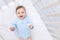 Happy smiling baby boy in crib in blue bodysuit, cute joyful little baby in bedroom