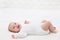 Happy Smiling Baby lying on back in White Bed. Active Playful Baby Boy in White Cotton Bodysuit. Laughing Infant Child in Onesies