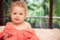 Happy smiling baby in soft pink blanket on white bed sheets in villa bedroom looking at camera with blurred tropical background