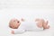 Happy Smiling Baby in White Cotton Onesies in Bed lying on Back Side View. Laughing Infant Child in babies Bodysuit play