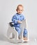 Happy smiling  barefooted baby boy in blue fleece jumpsuit with stars plays rides white kids rocking horse toy