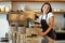 Happy smiling barista girl, korean bartender in apron, standing near coffee machine, prepare order for cafe client