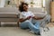 Happy smiling black woman sits on floor with smartphone cools herself with electric ventilator