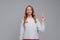 Happy smiling blonde woman pointing finger up, scolding or telling off someone, says: Attention please, wears white sweater, gray