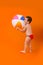 A happy smiling boy in bathing shorts holds an inflatable ball on an orange background