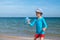 Happy smiling boy the European in a blue UF protective t-shirt and red shorts on the beach by the blue sea starts up soap bubbles