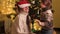 Happy smiling boy having fun and putting Santa hat on mother next to Christmas tree