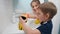 Happy smiling boy with mother wearing rubber gloves applying detergent and cleanser on sponges and washing bathroom