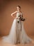 Happy smiling bride in ivory lace wedding dress with flattering tulle train and large cascade bridal bouquet on golden background