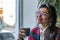 Happy smiling brunette business woman in glasses with red lips holds cup of coffe in hand and looking at the camera