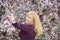 Happy smiling Caucasian blond woman with long hair near blossoming plum cherry tree, looking in the camera, slightly backward