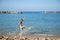 Happy smiling caucasian teenage girl in swimsuit makes splashes with her foot while walking along sea coast