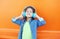 Happy smiling child enjoys listens to music in headphones over colorful orange