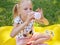 Happy smiling child girl drinking yogurt or milk outdoor at a summer picnic. Holding white plastic bottle and on face whiskers