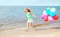 Happy smiling child on summer beach playing running with colorful balloons