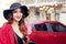 Happy smiling client woman in black hat near red car