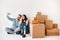 Happy smiling couple greeting friends at online video call using smartphone app sitting on floor surrounded by cardboard