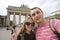 Happy smiling couple of tourists taking selfie photo on background of Brandenburg Gate in Berlin.