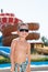 Happy smiling cute liitle boy in shorts and sunglasses in water park with water slides in summer