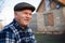 Happy smiling elder senior man portrait with a mustache in a cap on the background of a brick house in a Russian village